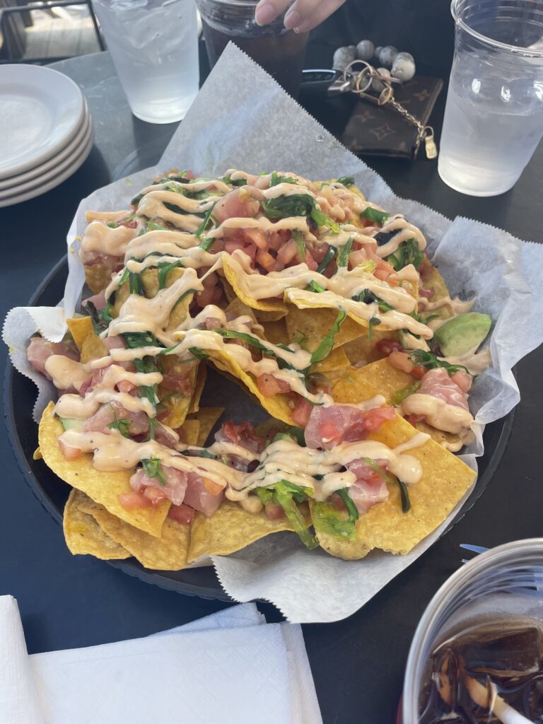 A plate of nachos topped with diced tomatoes, greens, and a creamy drizzle, served on a table