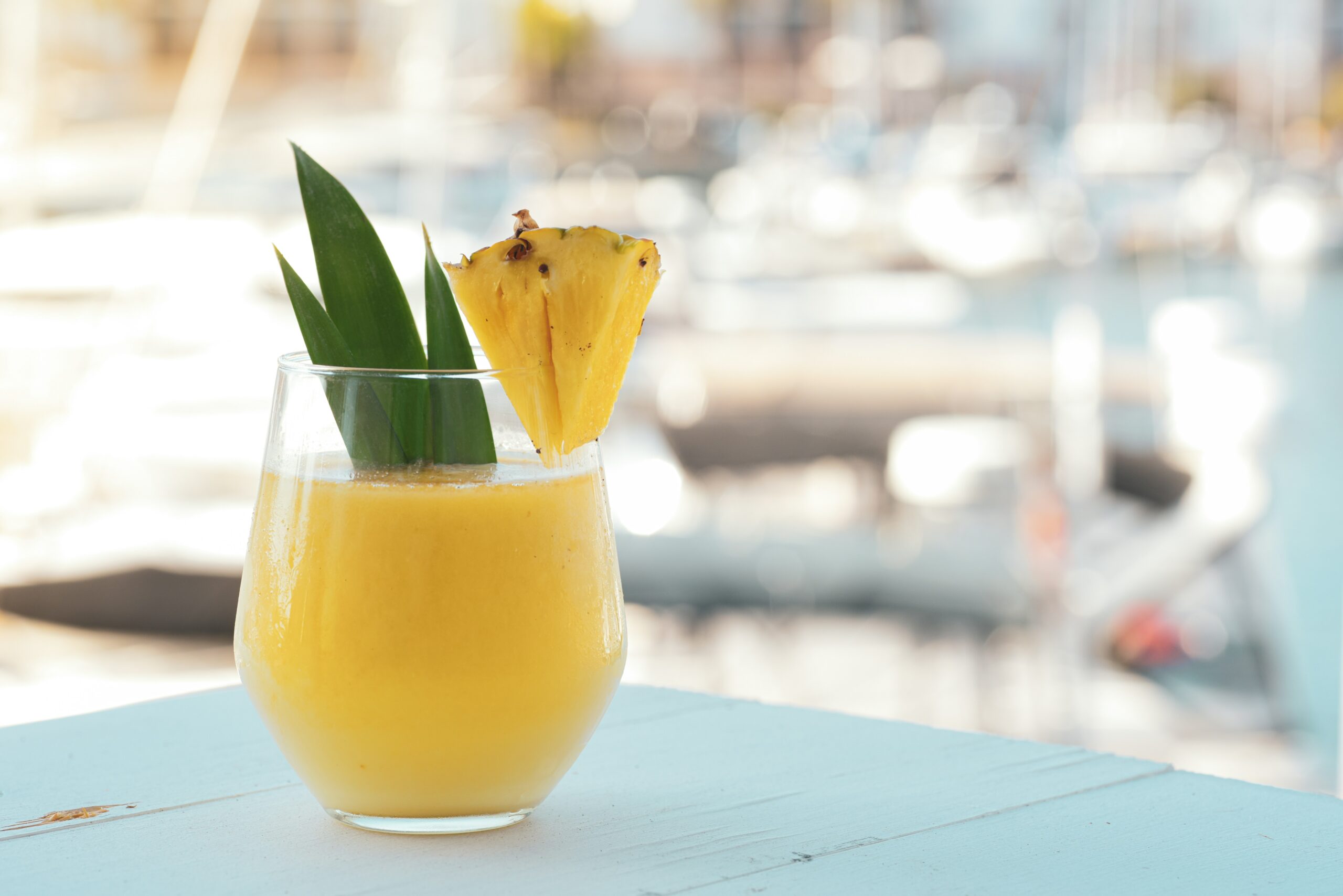 A Piña Colada on a blue table with a pineapple slice on the edge of the glass.